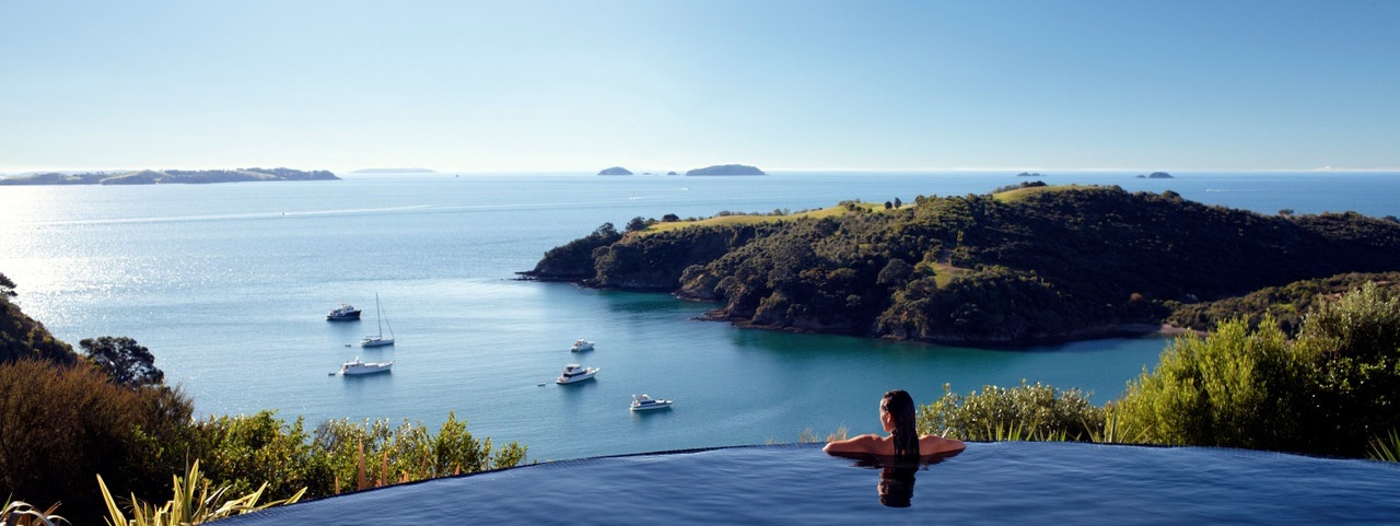 A woman at the edge of an infinity pool looking out to ocean and island views on Waiheke Island