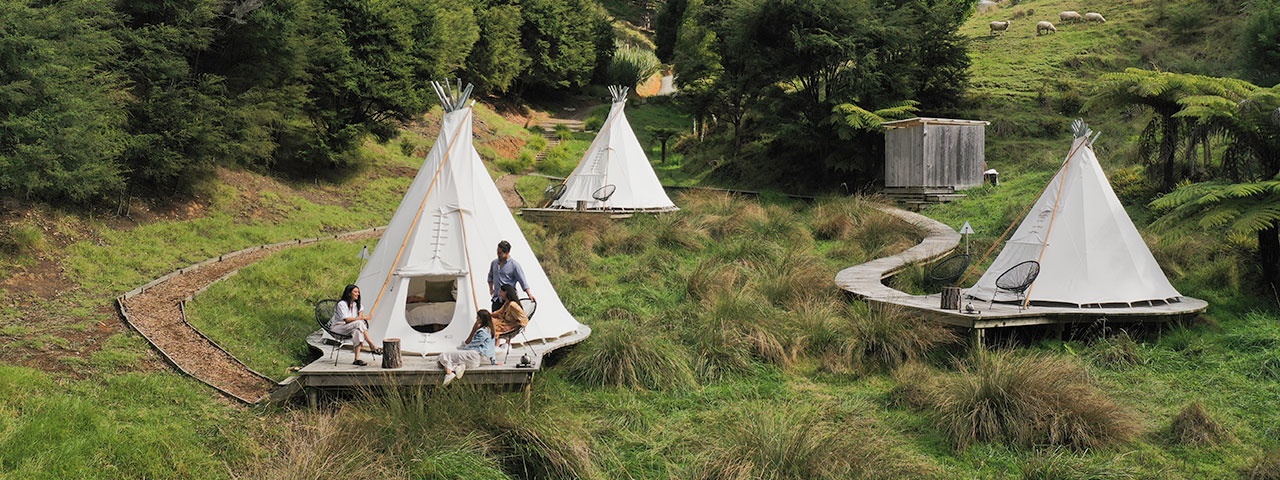 Three tepee tents with boardwalks around set on grassy hills with forest in the background