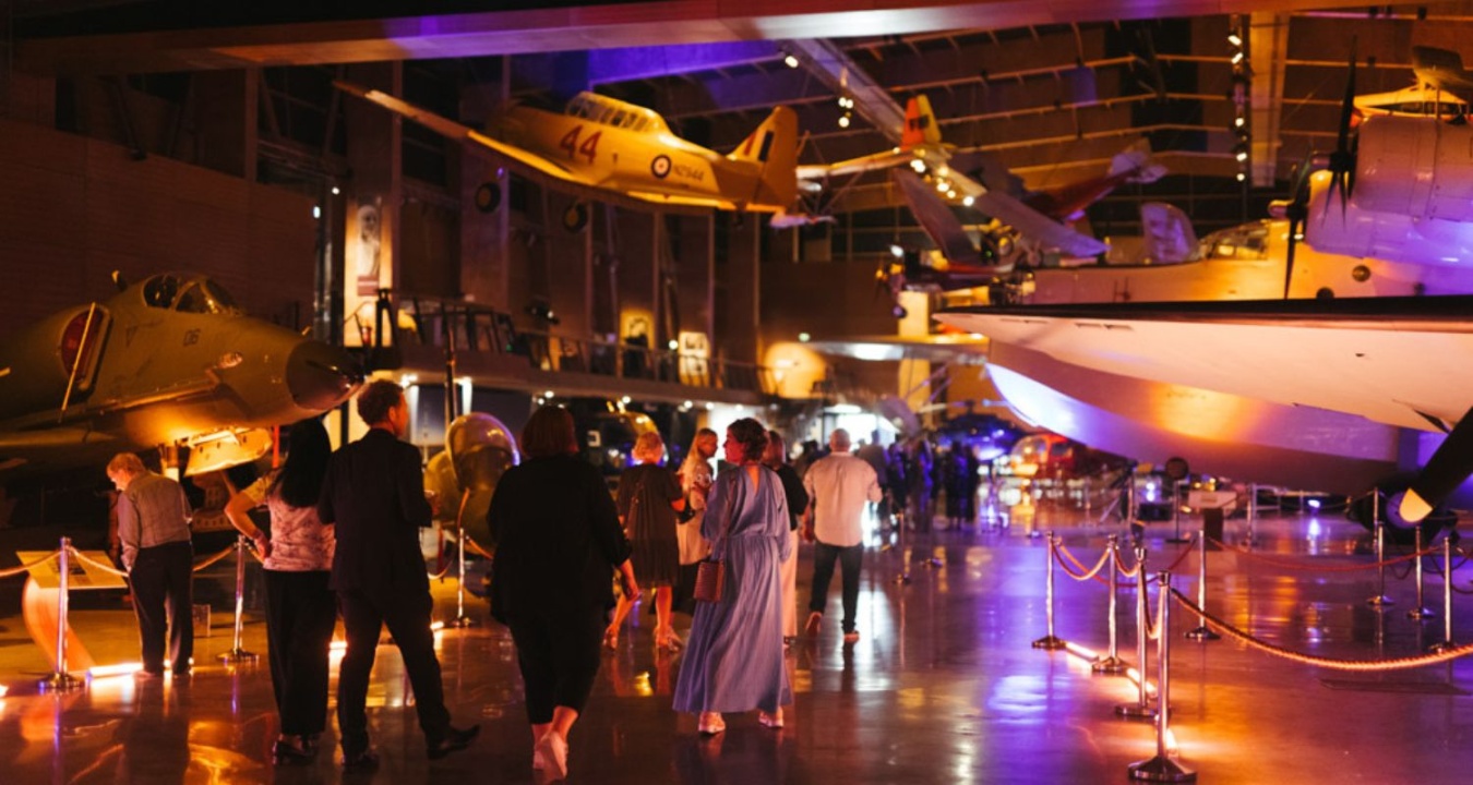 A group of people with their backs to the camera walking through the MOTAT aviation hall