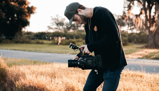 Man in black jacket and blue jeans holding a camera